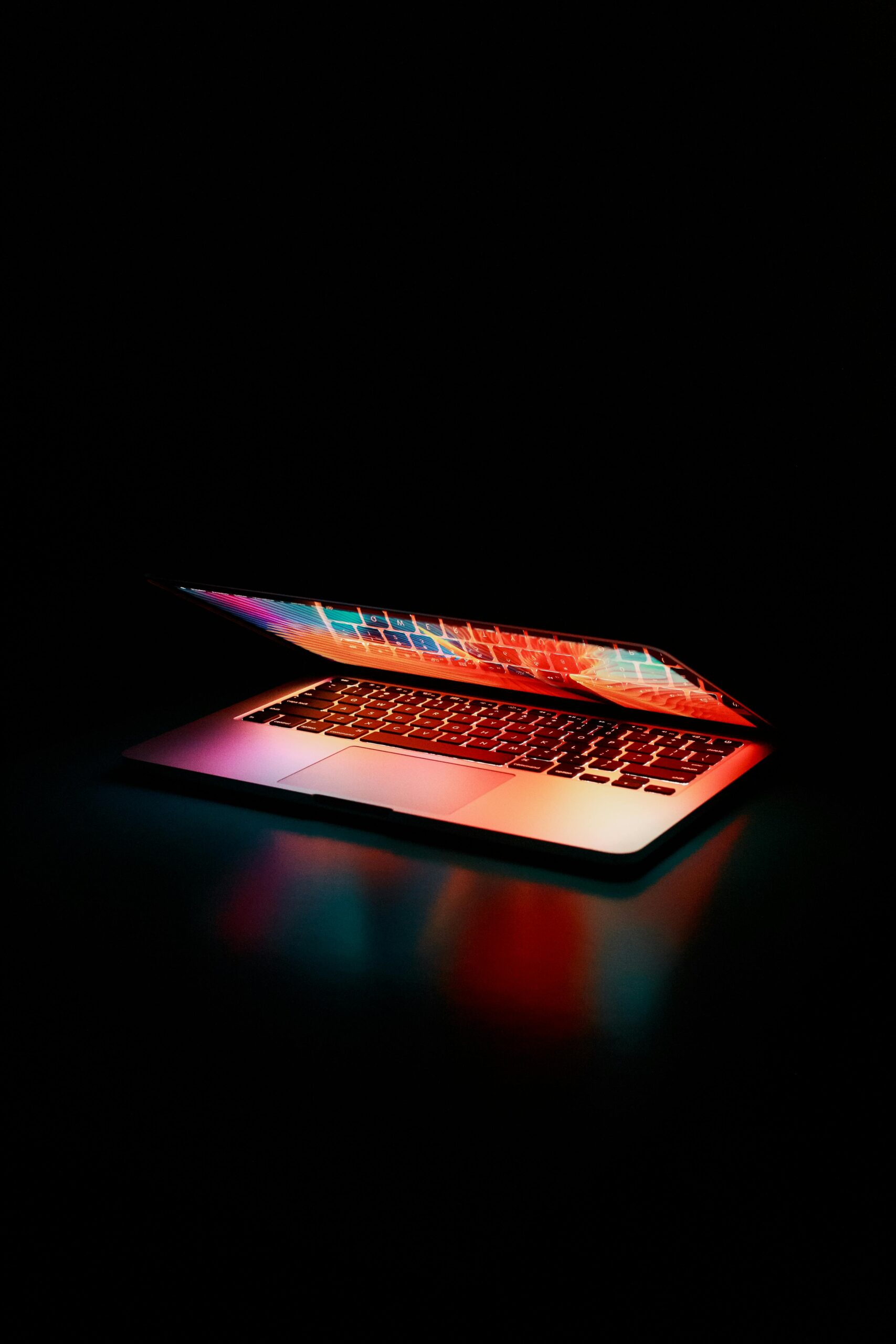 Categorías Laptop partially opened, emitting vibrant multicolored lights in dark setting.